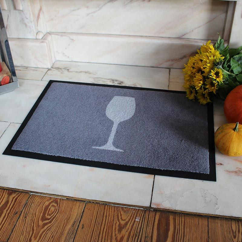 Produktfotos einer waschbare Fußmatte von Glücksmatte mit einem Weinglas in Hellgrau auf Dunkelgrau.