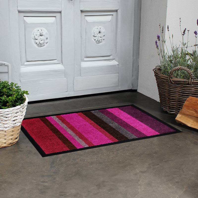 Fotomotiv der waschbare Glücksmatte Design-Fußmatte mit Streifen in Rosa vor einem Hauseingang.