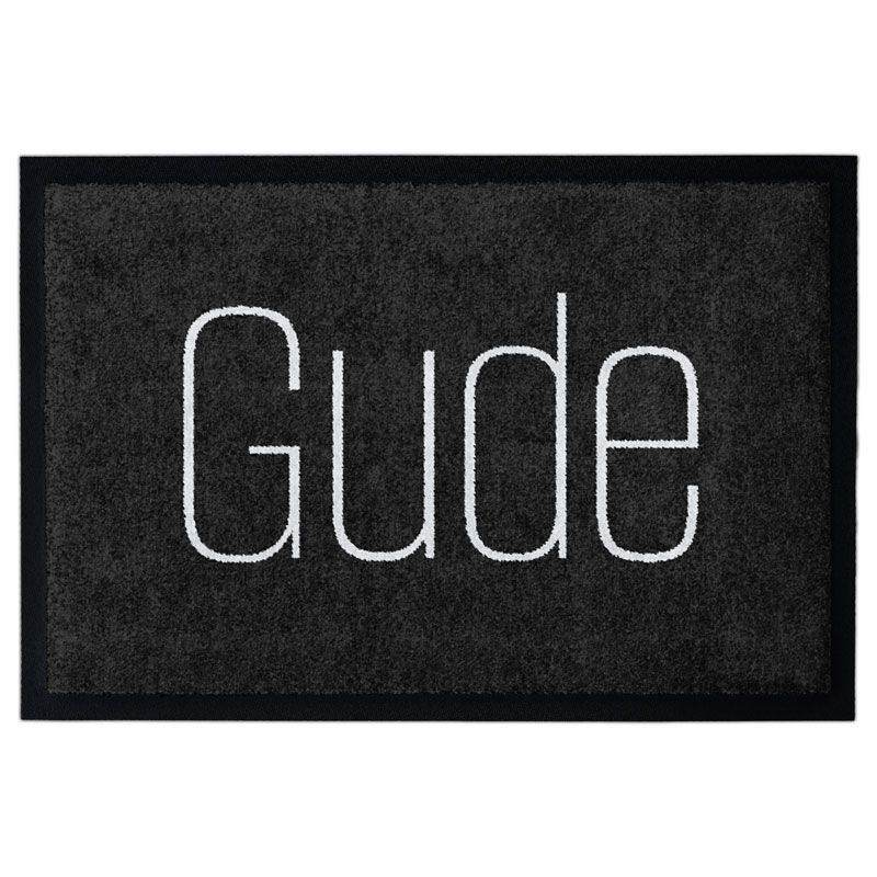 Waschbare Fußmatte von Glücksmatte mit dem Gruß "Gude" in moderner Schrift in Hellgrau auf Dunkelgrau. Mit Rand.