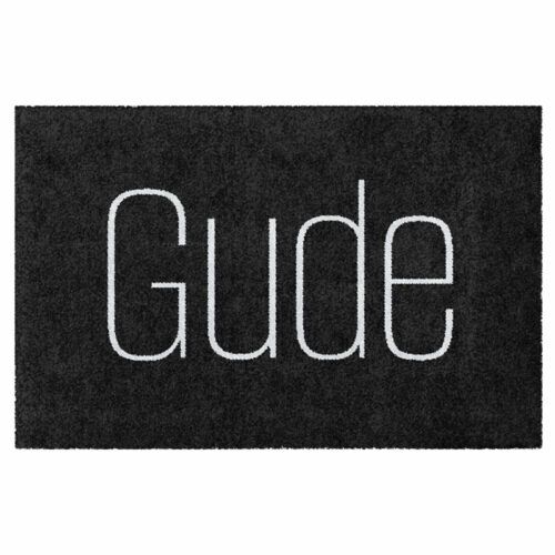 Waschbare Fußmatte von Glücksmatte mit dem Gruß "Gude" in moderner Schrift in Hellgrau auf Dunkelgrau. Ohne Rand.