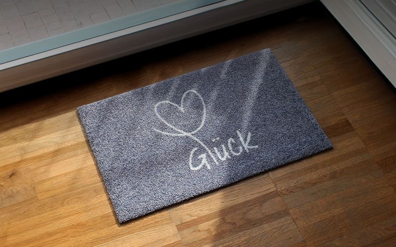 Glücksmatte-Fußmatte mit einem Hellgrauen Herz auf dunkelgrauem Hintergrund und der Aufschrift "Glück"