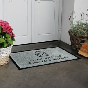 Personalisierte Fußmatte „Kleines Haus“ in Grau mit schwarzem Text und Hausmotiv und Mustertext "Hier wohnt Familie Klein".